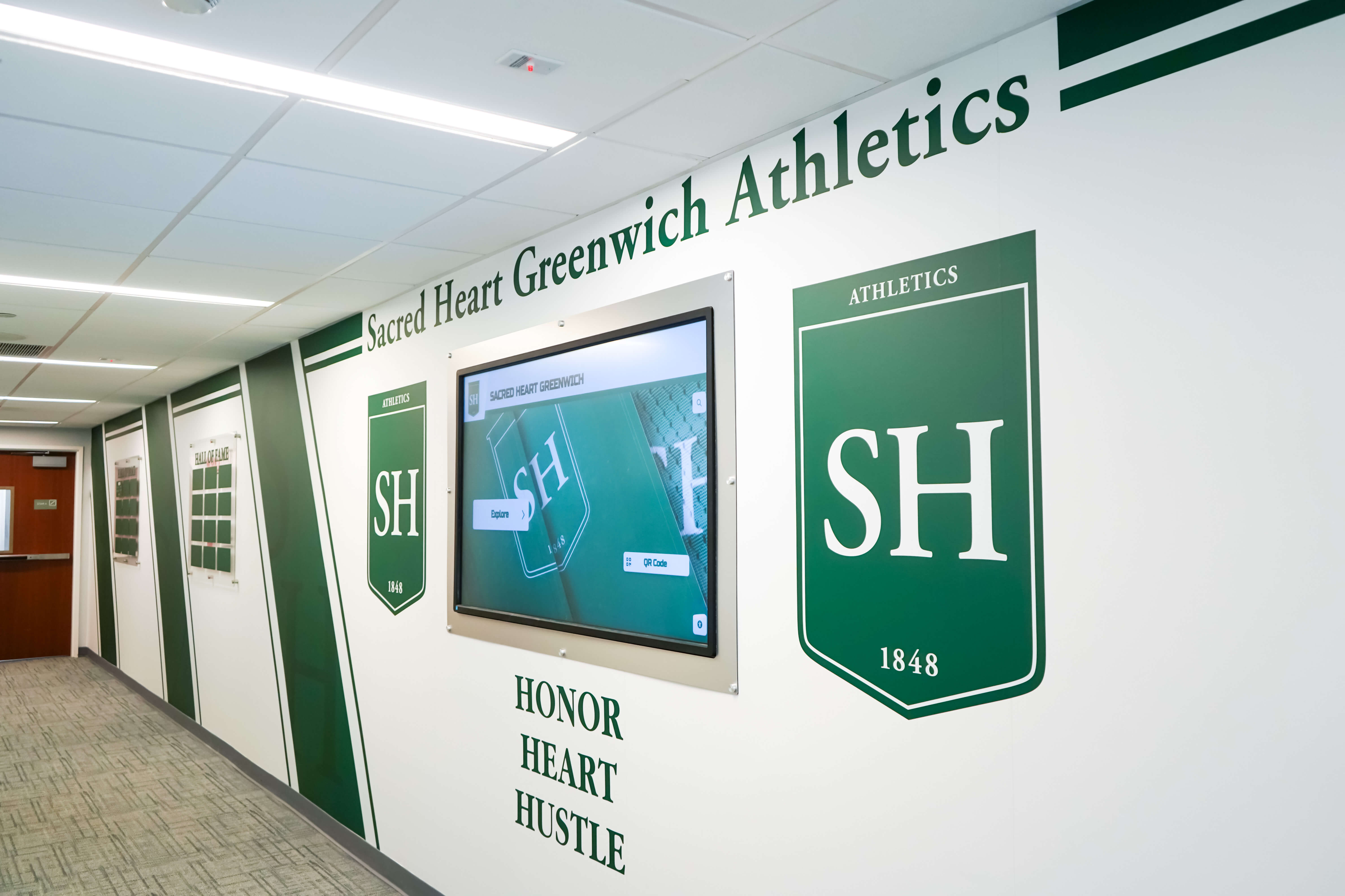 School athletics hallway with shield display honoring team achievements across multiple seasons Sacred Heart Greenwich athletics hallway shield display recognizing team achievements and program history