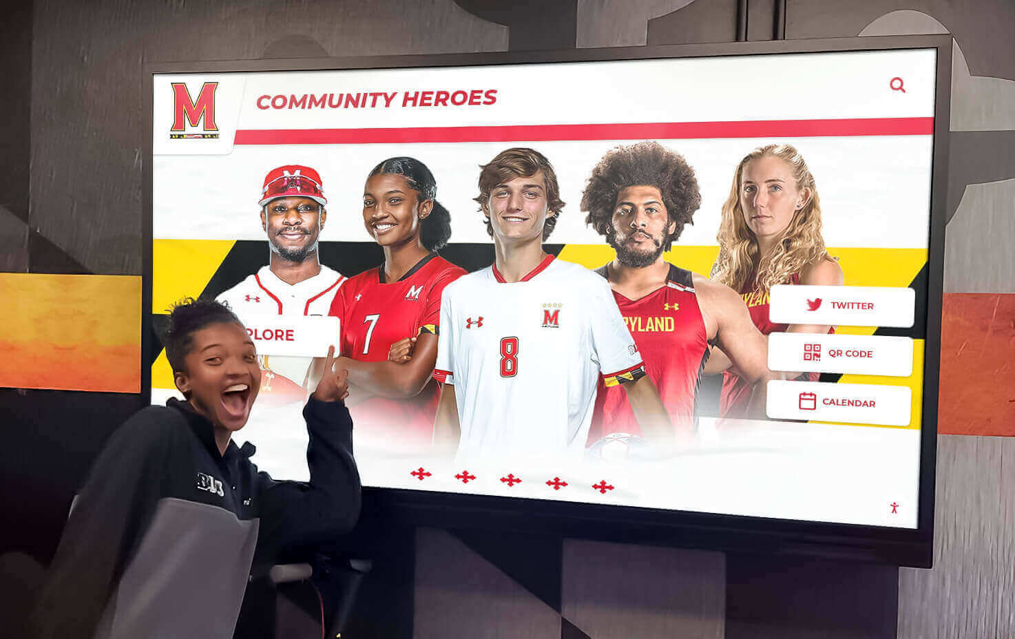 Student interacting with digital Community Heroes athletic display Student pointing at digital community heroes display