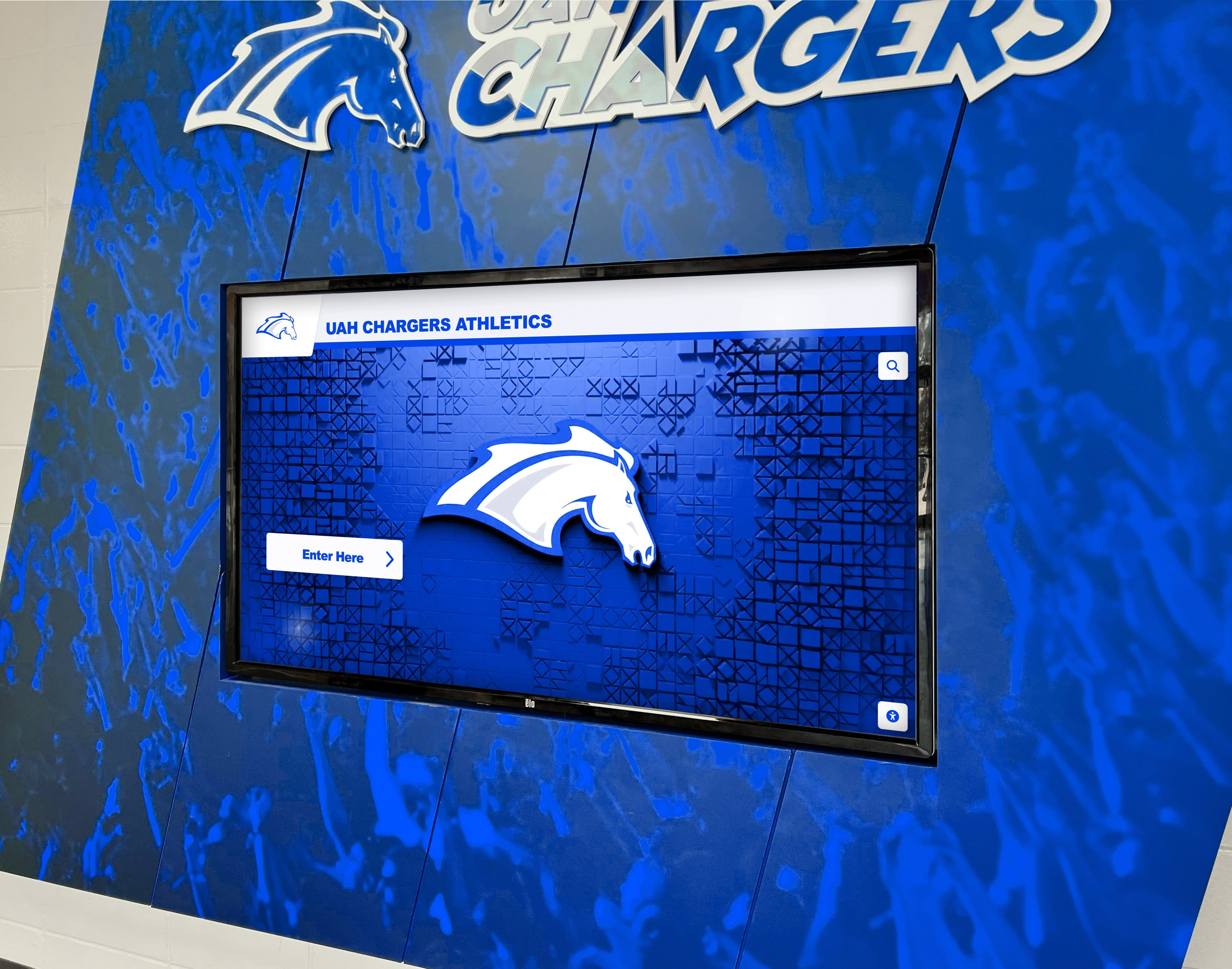 UAH Chargers athletics digital display screen mounted on blue wall in athletic facility